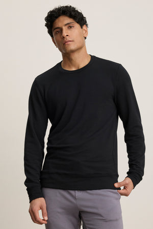 A man stands against a plain background wearing the SOREN PULLOVER by Velvet by Graham & Spencer and light gray pants, looking straight at the camera with a neutral expression.