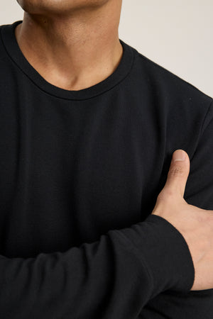 Wearing the SOREN PULLOVER by Velvet by Graham & Spencer, a person crosses their right arm over their chest, showing only their lower face and upper torso in the extra soft black long-sleeve shirt.
