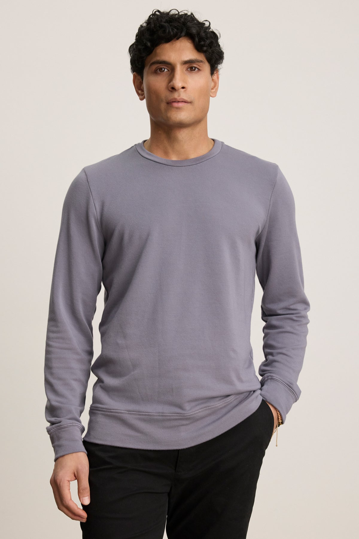 A man with short curly hair wears the SOREN PULLOVER by Velvet by Graham & Spencer in light purple and black pants, standing against a plain light background.-39841104756929