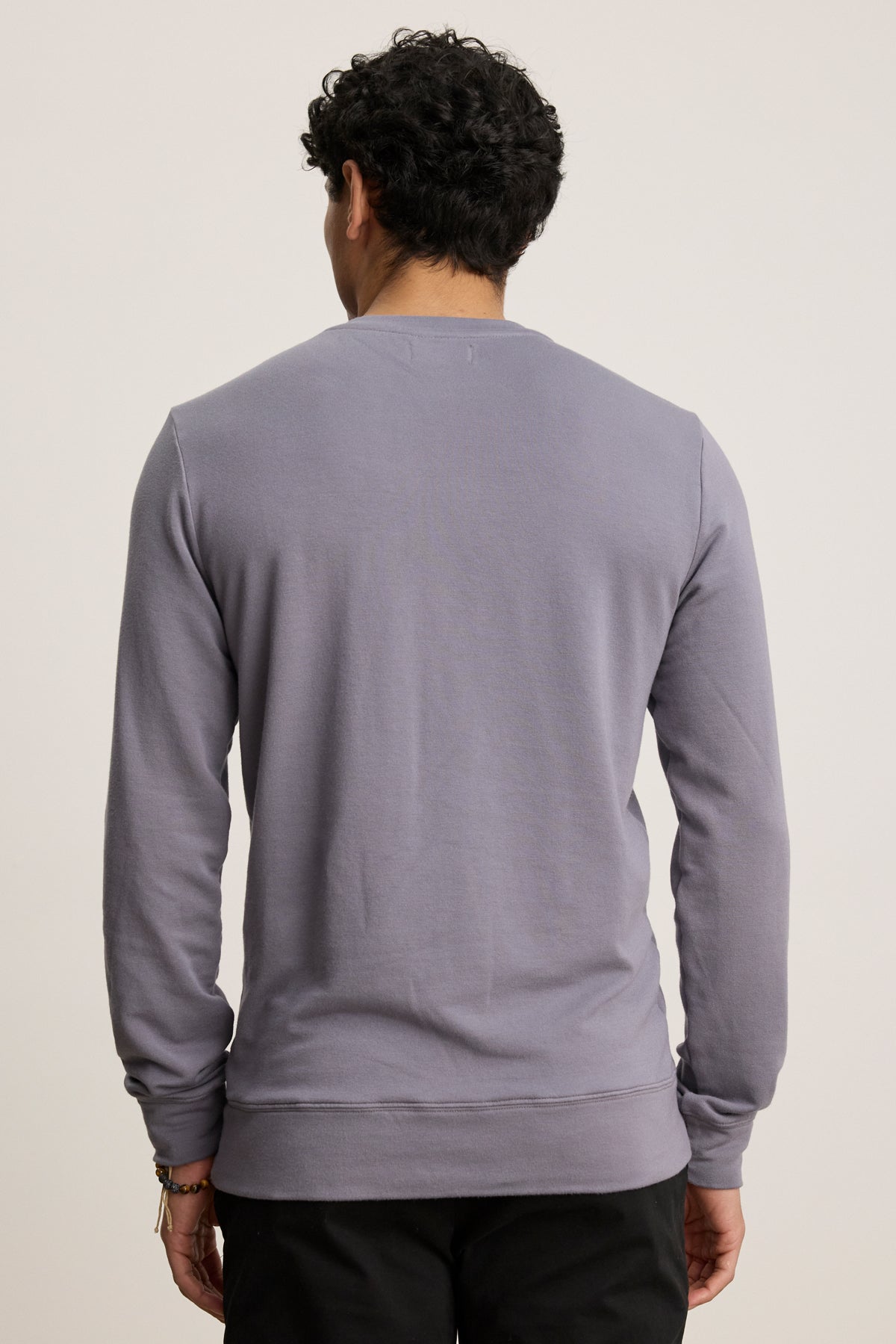 A person with short curly hair is shown from the back, wearing the Velvet by Graham & Spencer SOREN PULLOVER in light purple and black pants against a plain background.-39841104822465