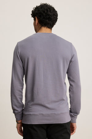 A person with short curly hair is shown from the back, wearing the Velvet by Graham & Spencer SOREN PULLOVER in light purple and black pants against a plain background.