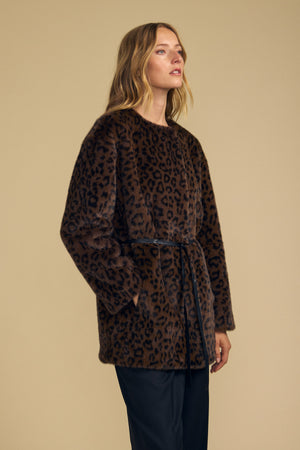 A woman wears the Velvet by Graham & Spencer MARMONT FAUX FUR JACKET, featuring a brown leopard print and detachable belt, standing against a plain beige background.