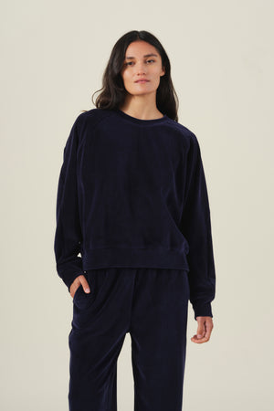 A woman wearing a dark blue CALLIE VELOUR SWEATSHIRT with matching long-sleeve loungewear pants.