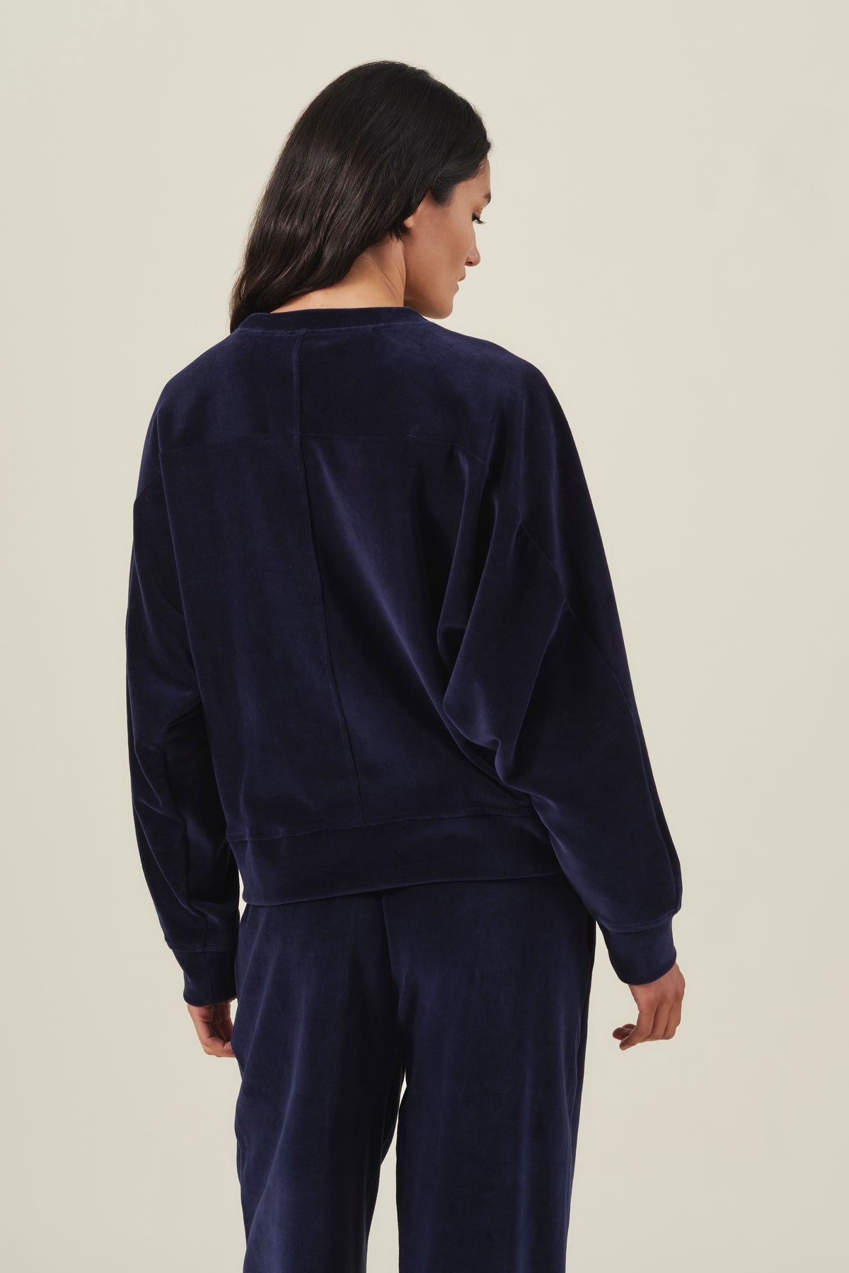 Back view of a person wearing a navy blue Velvet by Graham & Spencer CALLIE VELOUR SWEATSHIRT with a vertical seam down the center back.-46489865060545