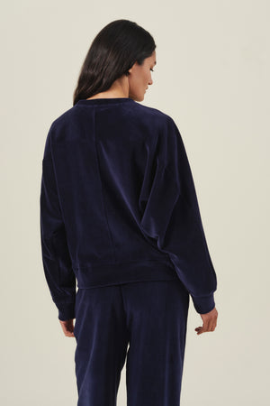 Back view of a person wearing a navy blue Velvet by Graham & Spencer CALLIE VELOUR SWEATSHIRT with a vertical seam down the center back.