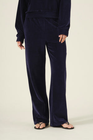 A person wearing a dark blue long-sleeved top and matching Velvet by Graham & Spencer DAISY VELOUR TRACK PANT wide-leg loungewear pants with flip-flops.