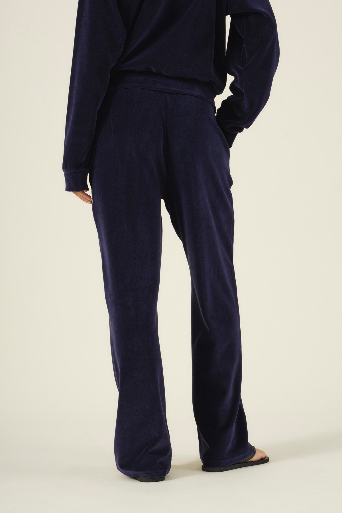 Rear view of a person wearing navy blue DAISY VELOUR TRACK PANT and a matching long-sleeve top with a plush feel.