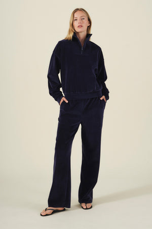 A woman wearing a matching navy blue long-sleeve quarter-zip pullover and DAISY VELOUR TRACK PANT plush velour track pants.