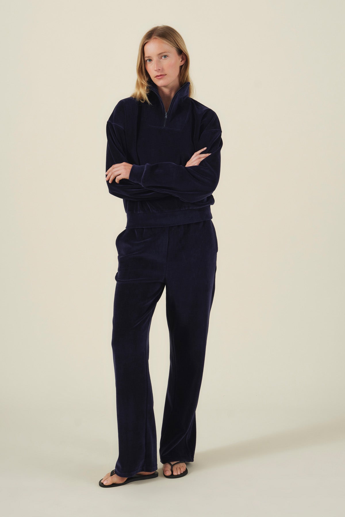 A person wearing a dark navy velour quarter-zip sweatshirt and matching DAISY VELOUR TRACK PANT with a plush, wide-leg fit.-46488220139713