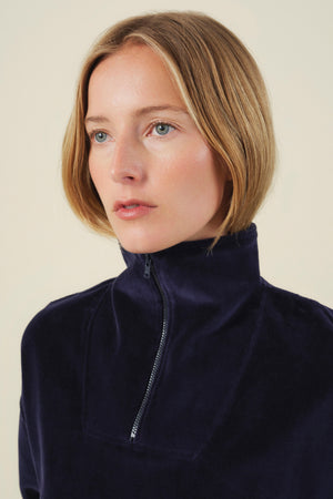A person wearing a navy blue DANICA VELOUR HALF-ZIP SWEATSHIRT with a mock neck and half-zip high collar.