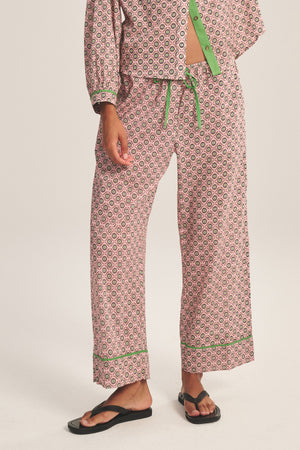 Someone wears the Velvet by Graham & Spencer MABEL PANT—patterned with contrast piping, green trim, and a matching drawstring waist—paired with black flip-flops, standing against a plain background.
