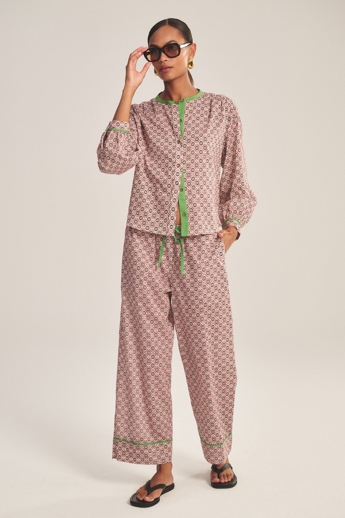 A woman in Velvet by Graham & Spencer's MABEL PANT, made from lightweight cotton voile with a relaxed leg and drawstring waist, stands against a plain background wearing black sandals and sunglasses, adjusting her glasses.-41088991985857