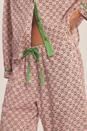 Close-up of a person wearing the Velvet by Graham & Spencer MABEL PANT—patterned pajamas with contrast piping and a green drawstring waist—showing part of their midriff with the shirt partly unbuttoned.