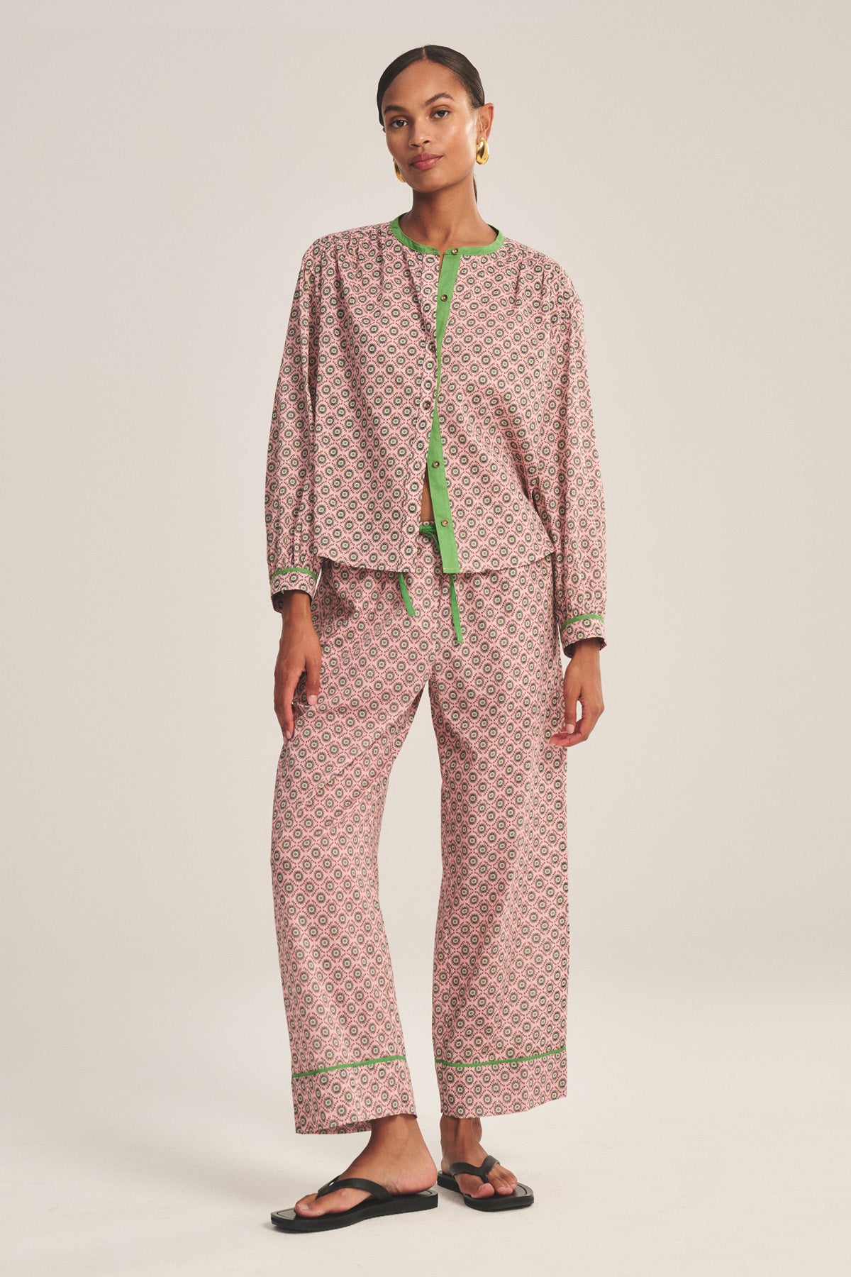 A woman stands against a plain background wearing the MABEL PANT by Velvet by Graham & Spencer, featuring a loose fit, pattern, drawstring waist, contrast piping, and paired with black sandals.