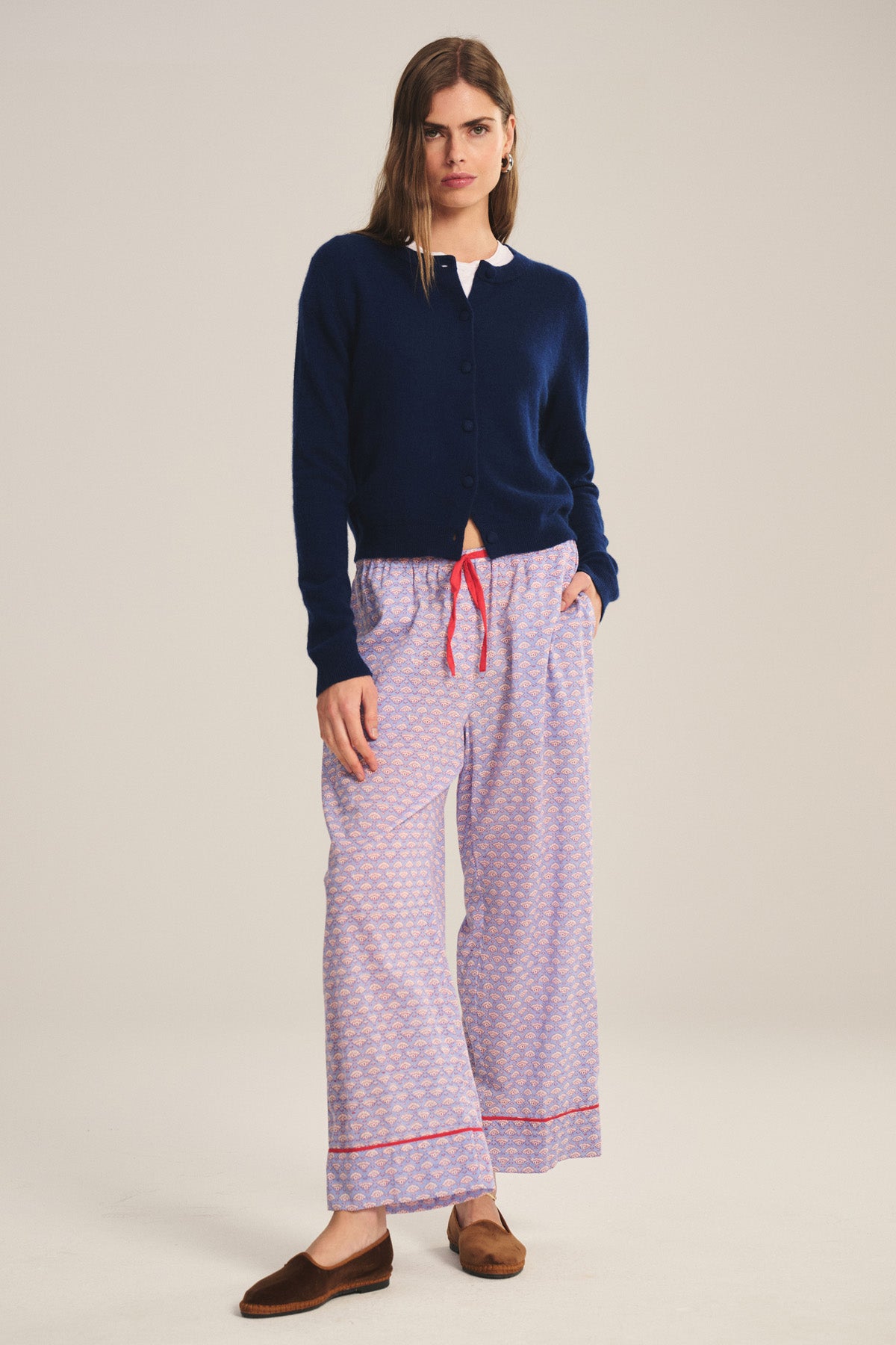 A woman wears Velvet by Graham & Spencer’s MABEL PANT—lightweight cotton with a drawstring waist and relaxed leg—paired with a navy blue cardigan, white shirt, and brown slippers against a plain backdrop.