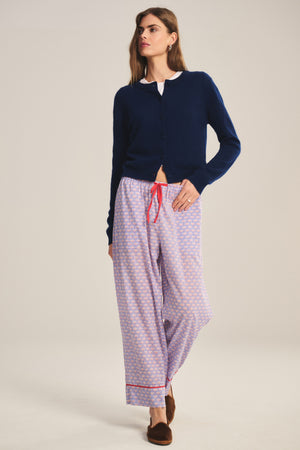 A woman stands against a plain background wearing Velvet by Graham & Spencer’s MABEL PANT, a lightweight cotton pant with a relaxed leg and red drawstring waist, paired with a navy cardigan, white shirt, and brown slippers.