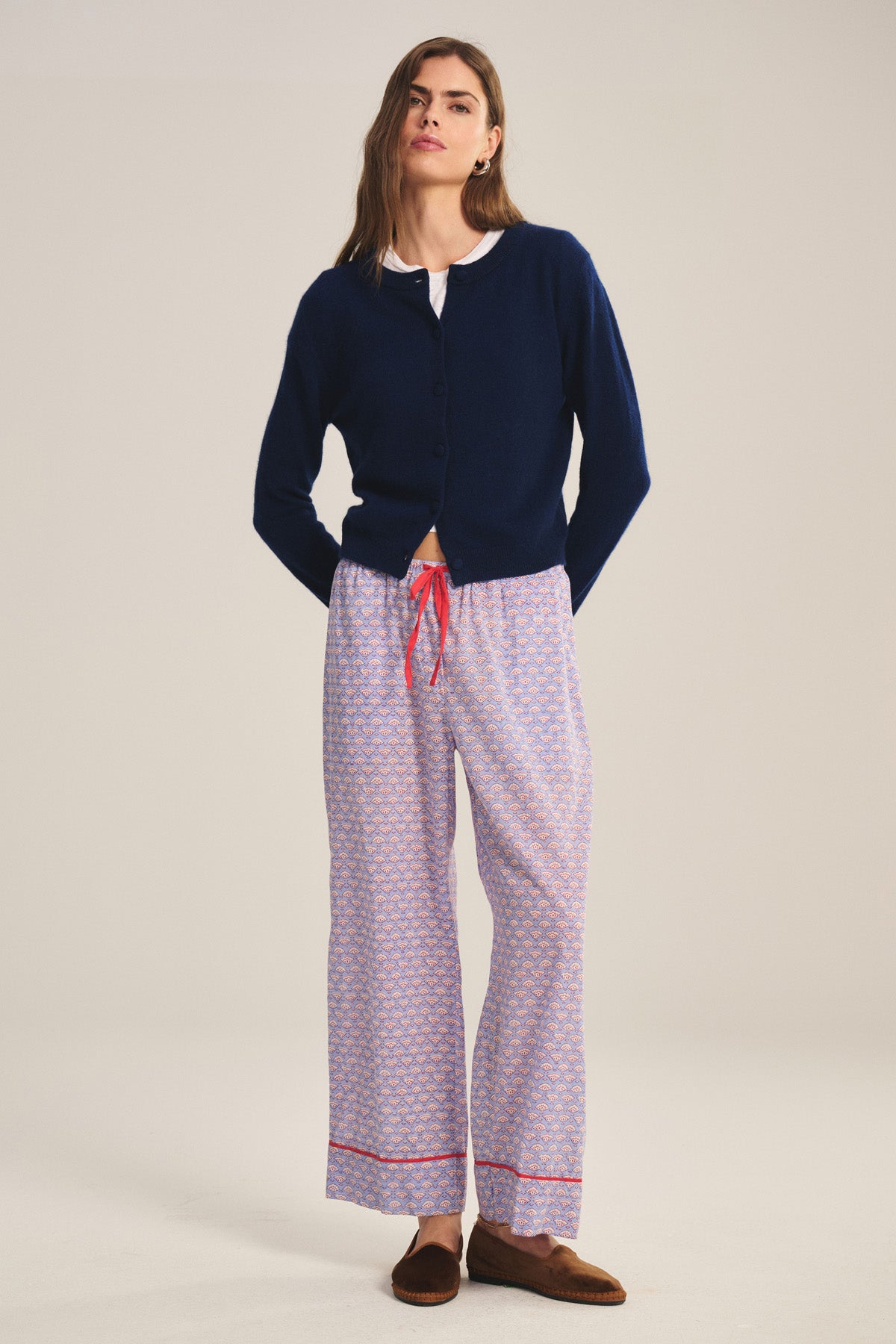 A person faces forward wearing the Velvet by Graham & Spencer MABEL PANT, a lightweight cotton pant with a drawstring waist and relaxed leg, styled with a navy cardigan, white shirt, and brown slippers against a plain background.