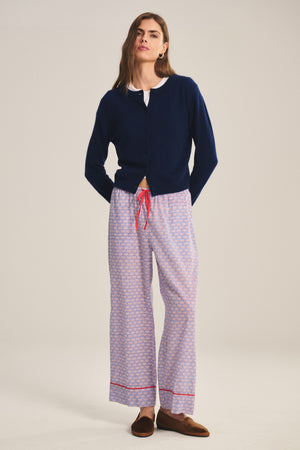 A person faces forward wearing the Velvet by Graham & Spencer MABEL PANT, a lightweight cotton pant with a drawstring waist and relaxed leg, styled with a navy cardigan, white shirt, and brown slippers against a plain background.