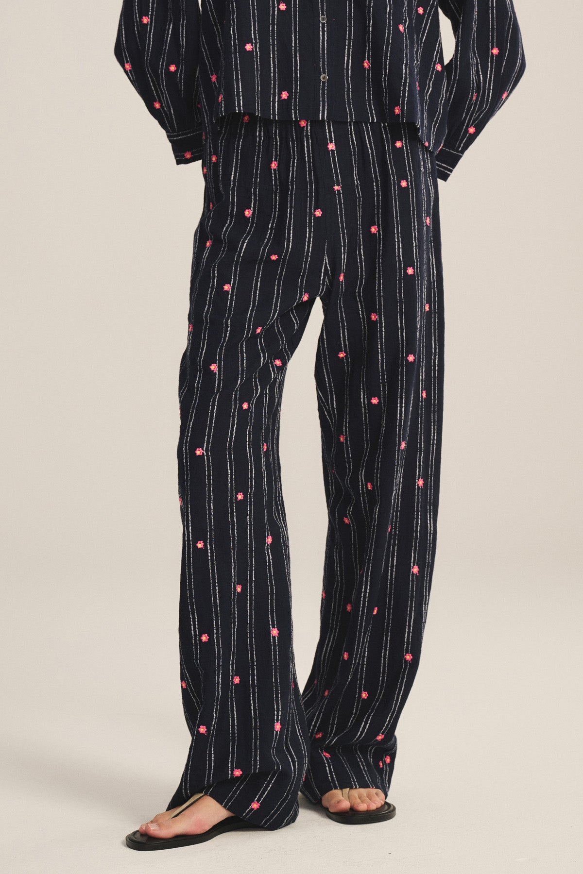 Model wearing Velvet by Graham & Spencer MADELYN PANT—relaxed fit black pants with vertical white stripes and pink dot patterns—paired with a matching top and black sandals.