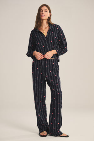 A woman models the MADELYN PANT by Velvet by Graham & Spencer—a relaxed fit, dark pajama-style set with white stripes and red dots—standing against a plain light background.