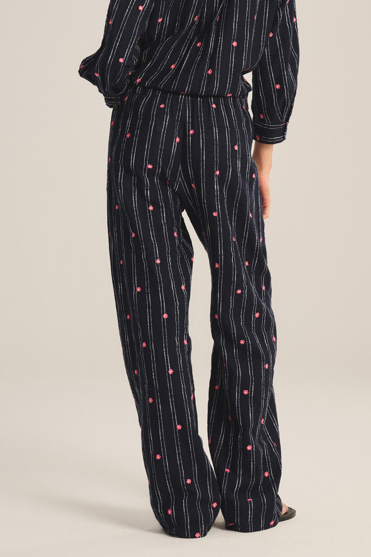 Model shown from the back wears the MADELYN PANT by Velvet by Graham & Spencer—relaxed fit, dark pajama pants with vertical white stripes and small pink dots, posed against a light background.-41296887480513