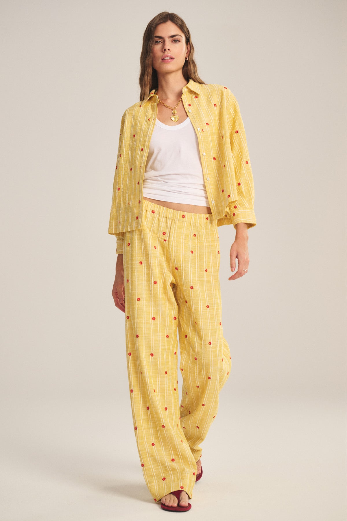 A woman models the MADELYN PANT by Velvet by Graham & Spencer, a yellow plaid pajama with red dots and a relaxed straight-leg fit, styled with a white tank top and red sandals against a plain backdrop.-41128095645889