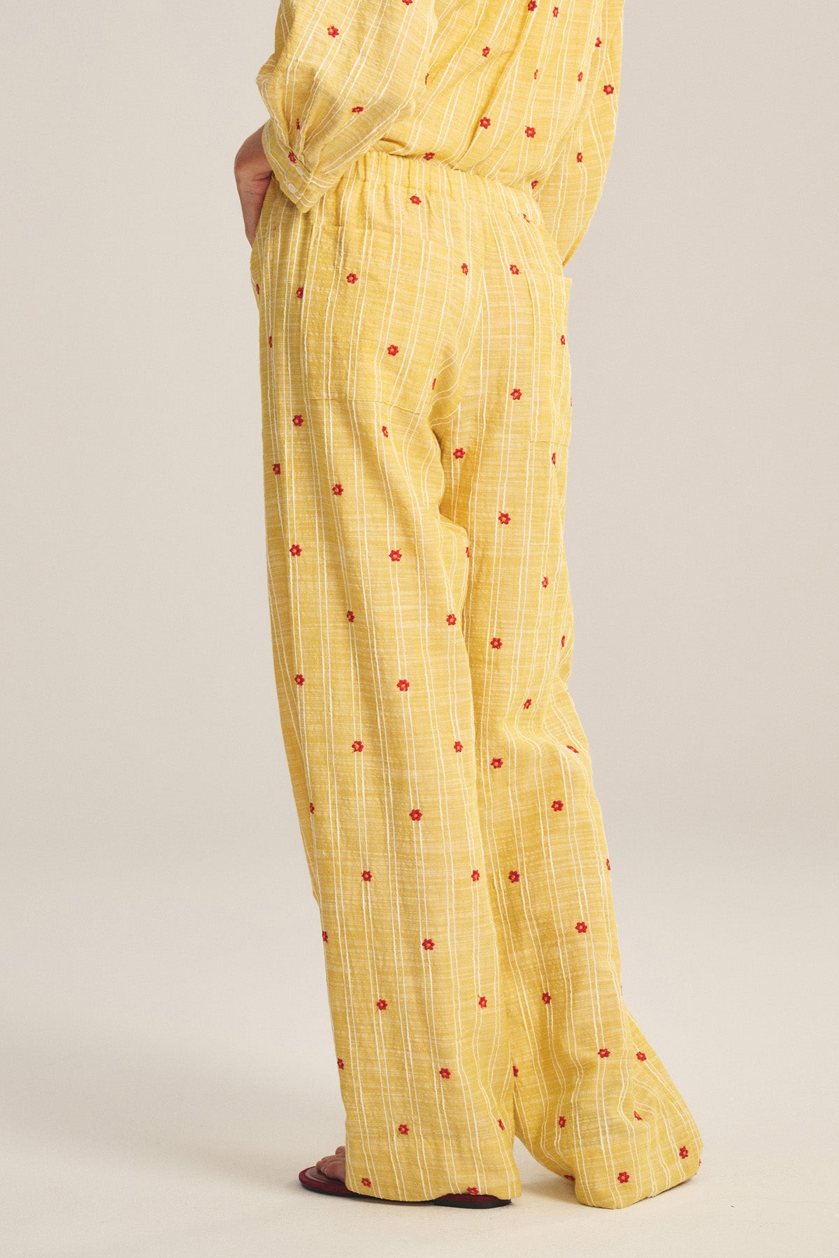 Model wears Velvet by Graham & Spencer MADELYN PANT: relaxed-fit yellow pants with subtle plaid, small red flowers, straight-leg style, waist-down side view.-41128095514817