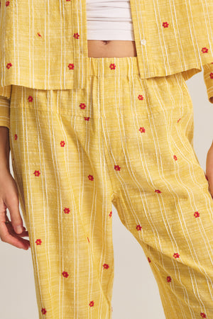 Model shown from midsection down wearing the MADELYN PANT by Velvet by Graham & Spencer, a relaxed fit yellow pant with white stripes and small red floral patterns, featuring a straight-leg silhouette.