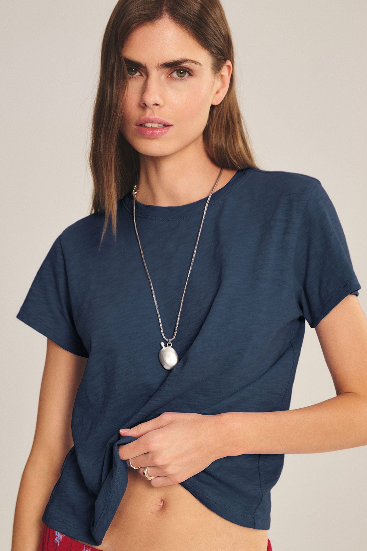 A woman with long brown hair wears a Velvet by Graham & Spencer MARIKA TEE in dark blue cotton slub with a relaxed boxy fit, styled with a silver pendant necklace and posing against a neutral backdrop.-40183825400001