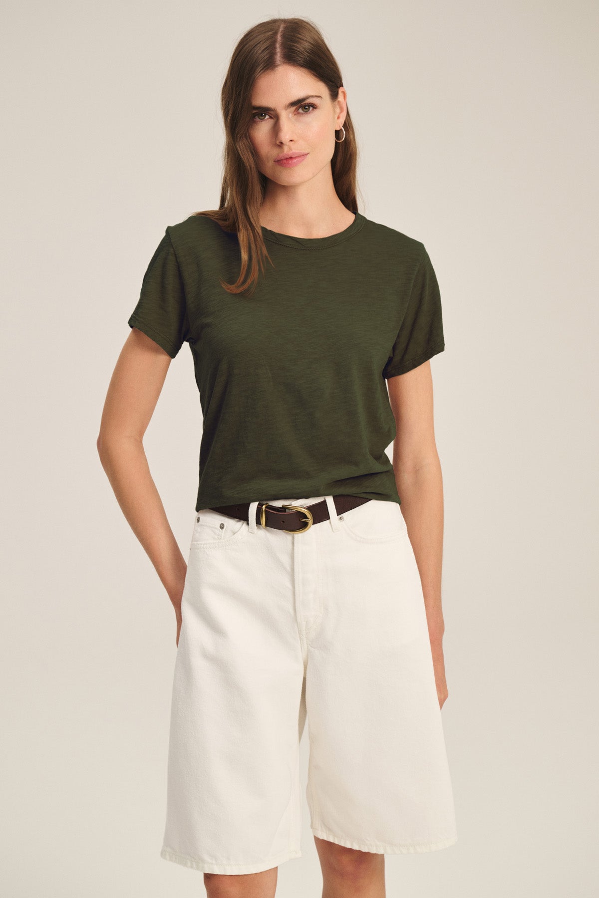 A woman wears the MARIKA TEE by Velvet by Graham & Spencer in dark green, featuring a relaxed boxy fit, tucked into high-waisted, knee-length white shorts with a dark belt.-40825912197313