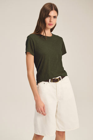 A woman wears the MARIKA TEE by Velvet by Graham & Spencer in dark green, styled with high-waisted knee-length white shorts and a black belt, standing against a plain background.