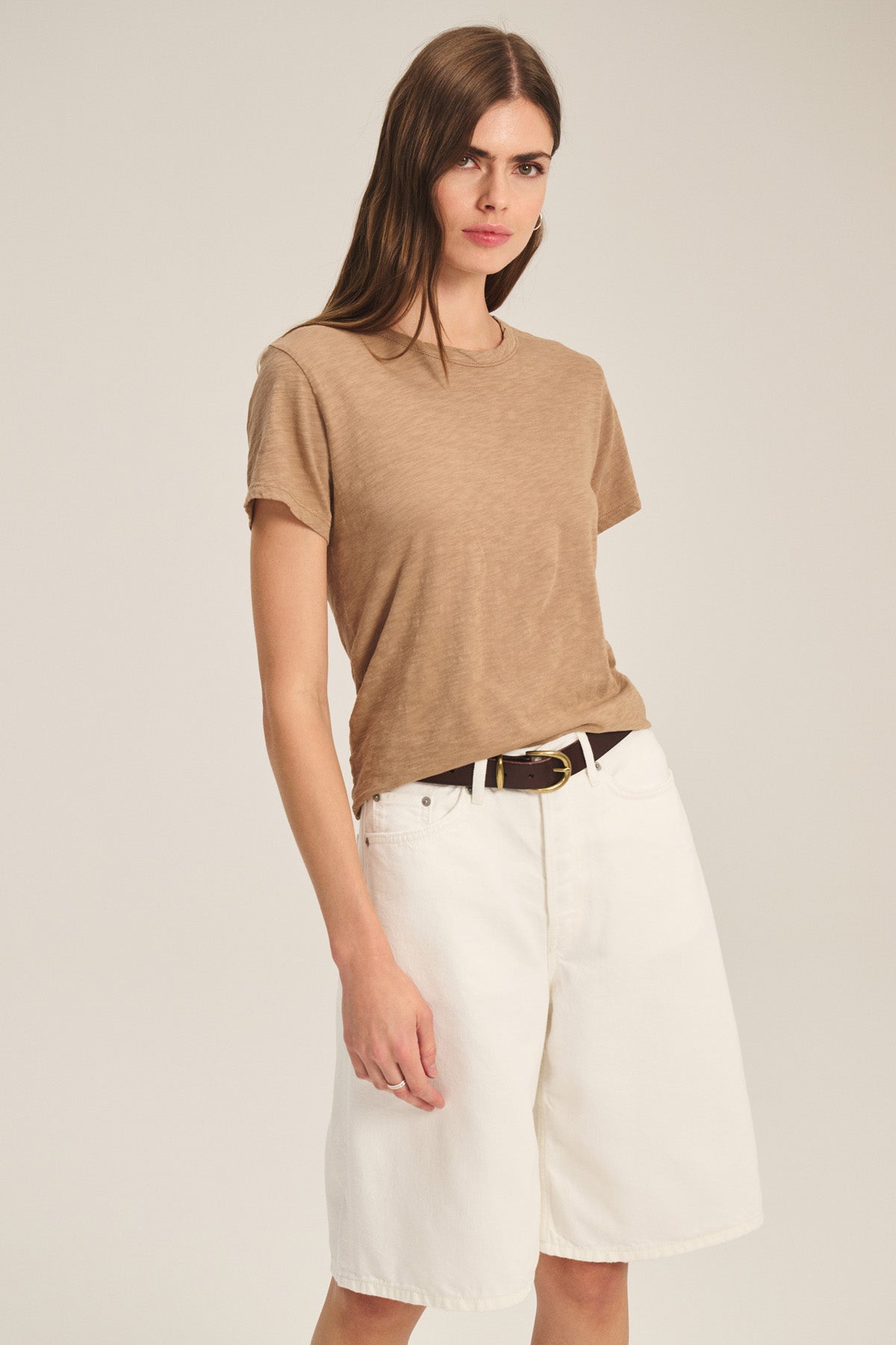A woman wears the light brown MARIKA TEE by Velvet by Graham & Spencer, tucked into high-waisted, loose white shorts with a black belt, standing against a plain background.
