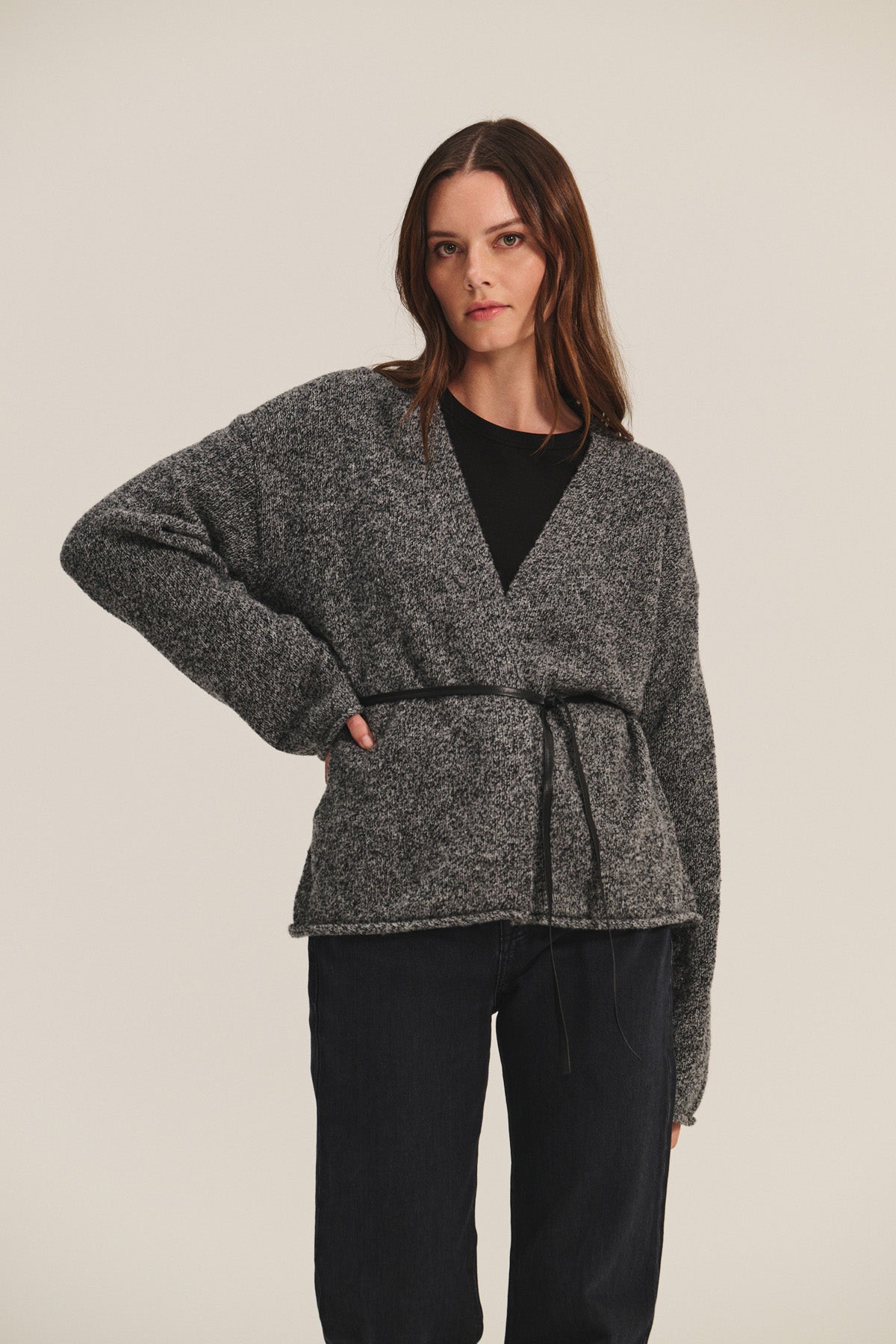 A woman faces forward in the ALINA CARDIGAN by Velvet by Graham & Spencer, a wool blend wrap with a belt, styled over a black top and dark pants, showcasing a relaxed silhouette against a plain light background.