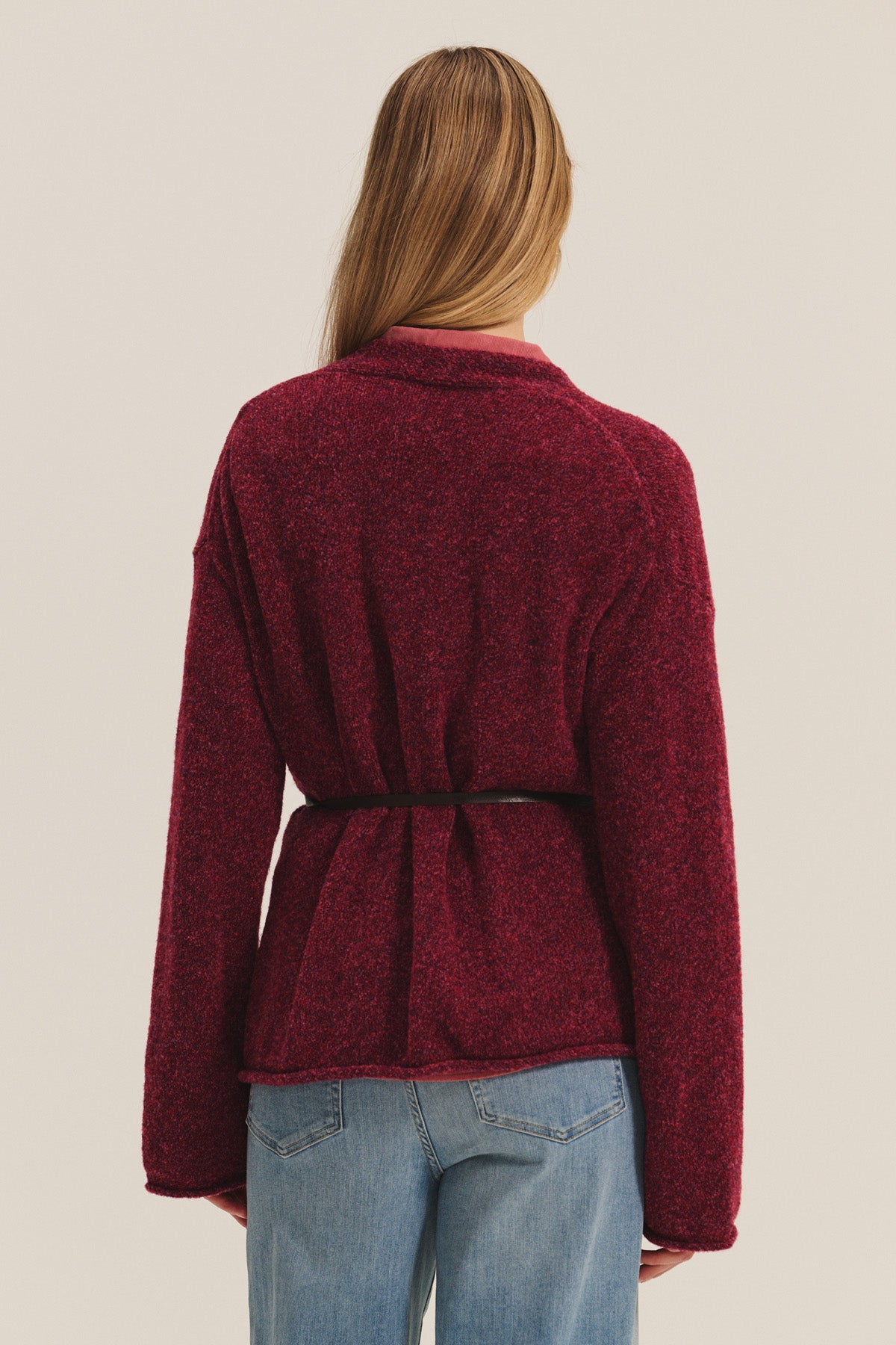 A person with long, light brown hair wears the Velvet by Graham & Spencer ALINA CARDIGAN in red, belted at the waist with blue jeans. Shown from the back against a plain background, the relaxed fit creates a casually elegant look.