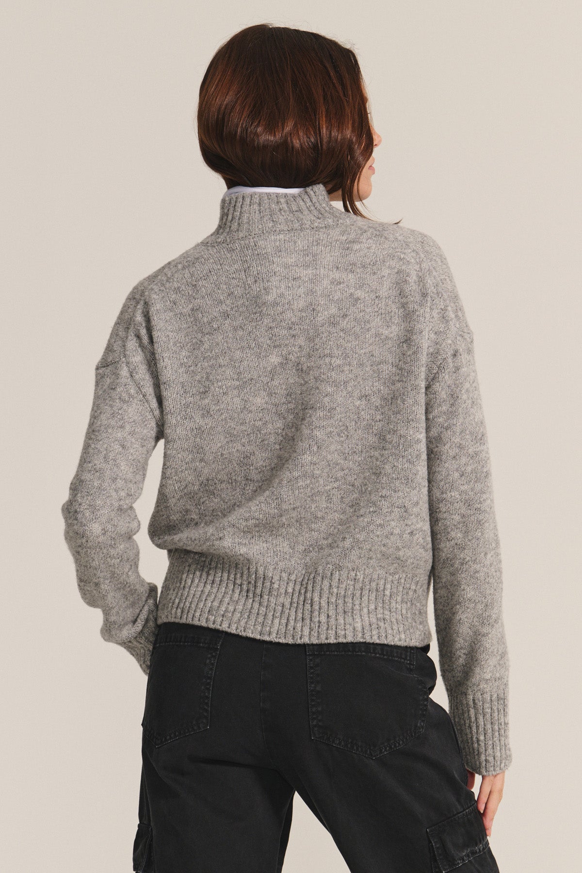 A person with brown hair wears the BRIELLE SWEATER by Velvet by Graham & Spencer, a gray wool blend turtleneck, paired with black pants and shown from the back against a plain background.-40333255311553