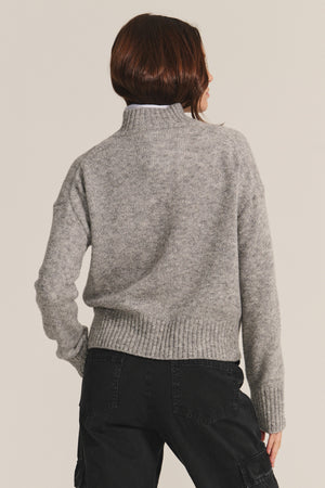 A person with brown hair wears the BRIELLE SWEATER by Velvet by Graham & Spencer, a gray wool blend turtleneck, paired with black pants and shown from the back against a plain background.