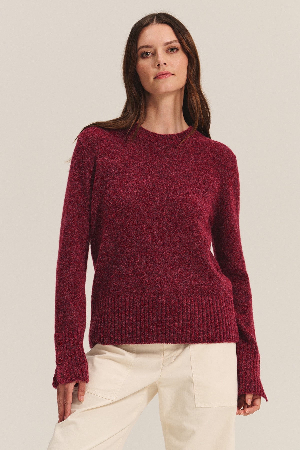 A woman models the MAISIE SWEATER by Velvet by Graham & Spencer, a long-sleeve dark red wool blend with ribbed cuffs, crew neckline, and hem, styled with off-white pants against a simple light background.