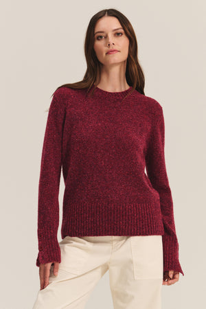 A woman models the MAISIE SWEATER by Velvet by Graham & Spencer, a long-sleeve dark red wool blend with ribbed cuffs, crew neckline, and hem, styled with off-white pants against a simple light background.