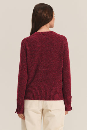 A person with long brown hair is shown from the back, wearing the MAISIE SWEATER by Velvet by Graham & Spencer—a textured maroon crew neck—paired with cream pants, creating a versatile cold-weather look against a neutral background.