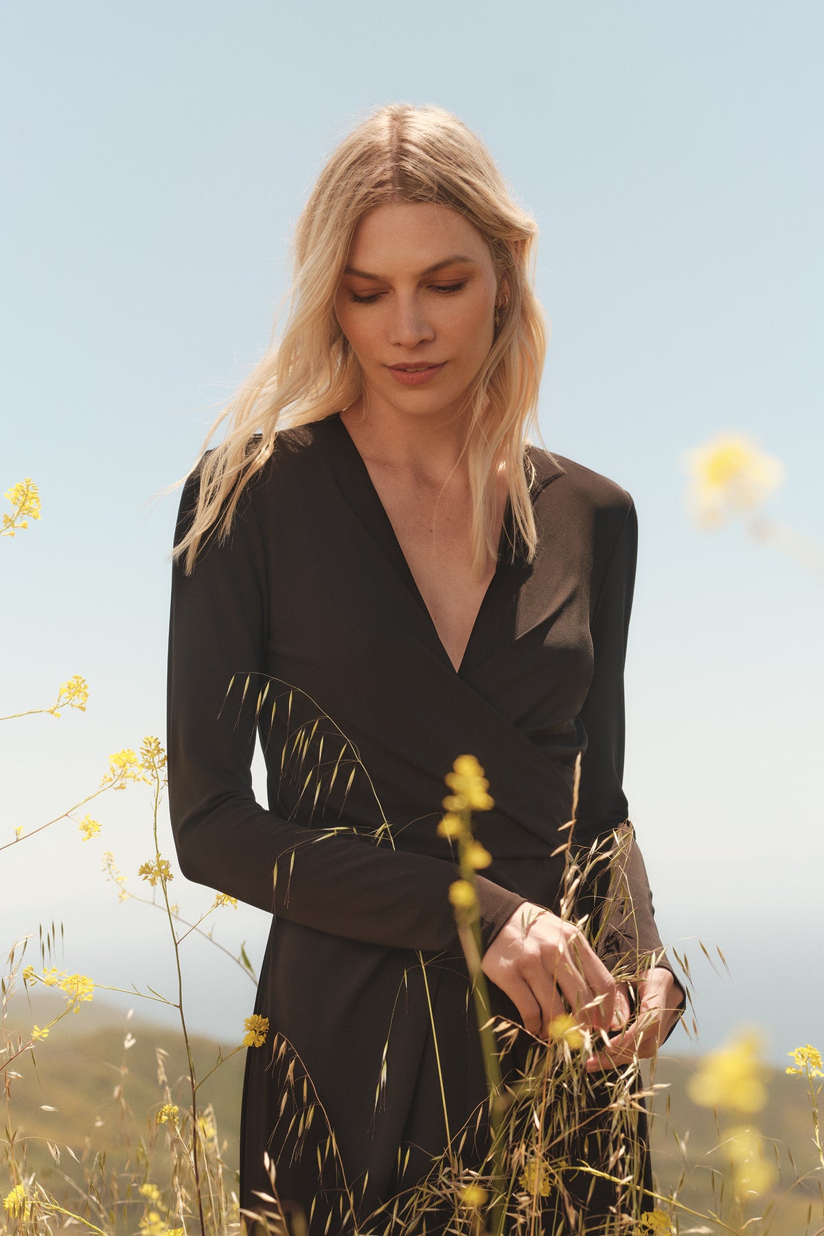   A blonde woman in a Velvet by Graham & Spencer ELIANA WRAP MIDI DRESS standing in a field. 