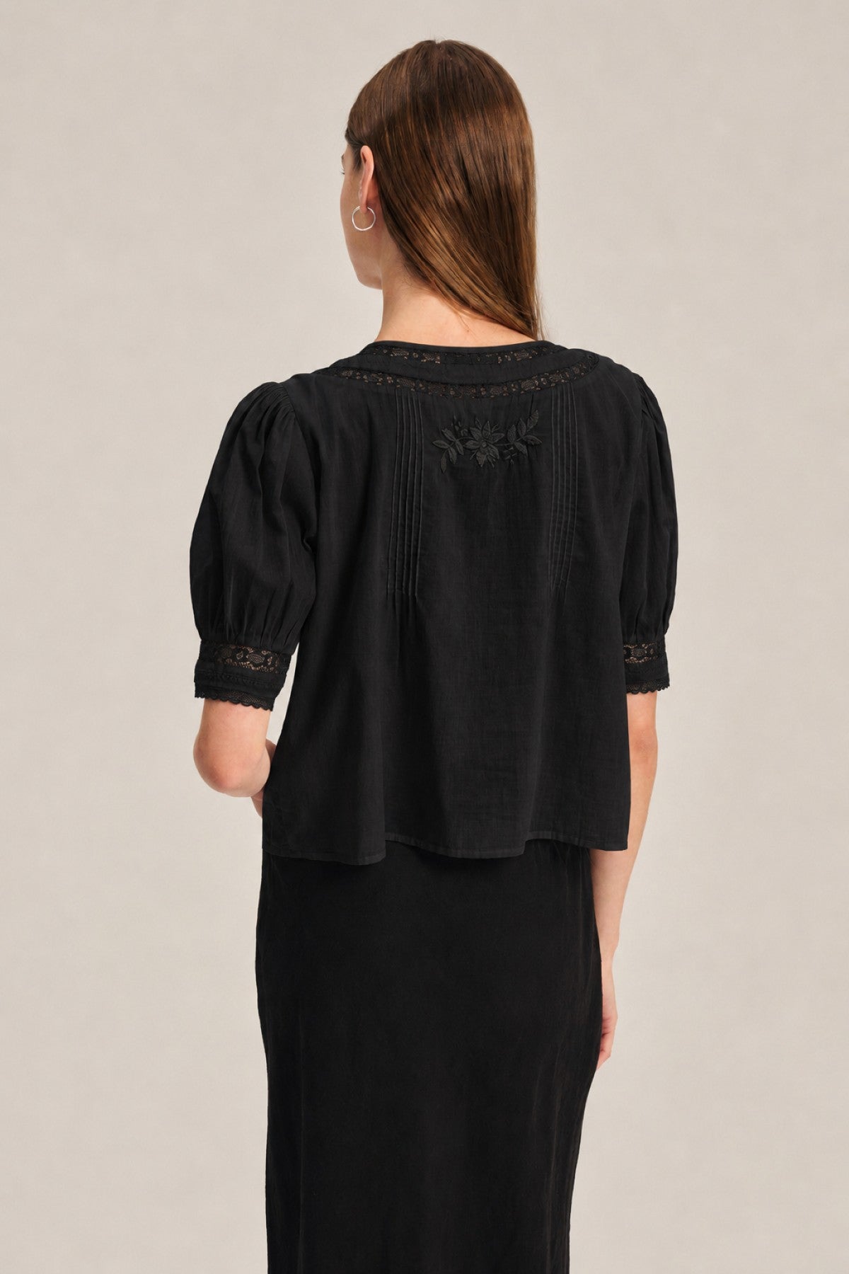 A person with straight brown hair wears the MAVIS TOP by Velvet by Graham & Spencer—a feminine sheer black short-sleeve top with lace and delicate embroidery—shown from the back.-41706513563841