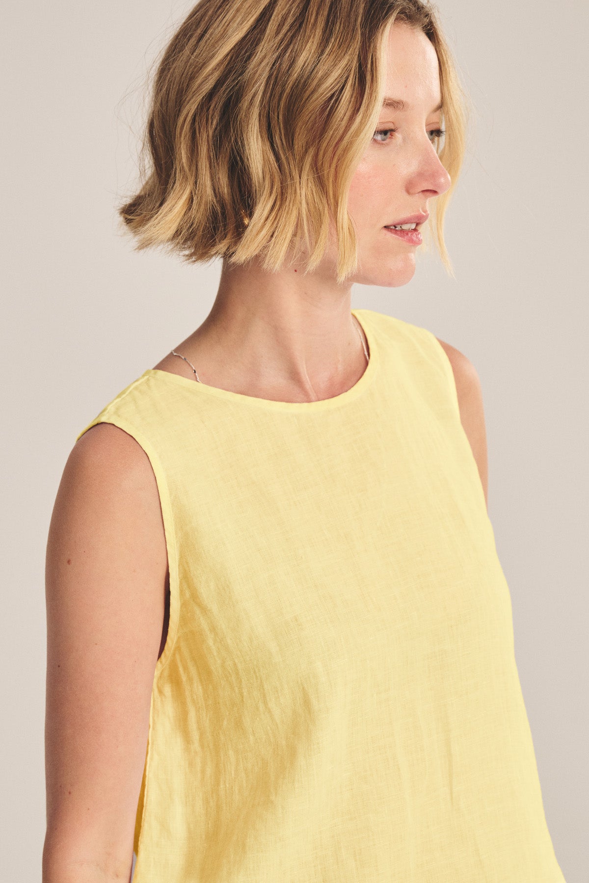 A woman with short blonde hair is wearing the MAXINE LINEN TOP by Velvet by Graham & Spencer in yellow, looking to the side against a neutral background.