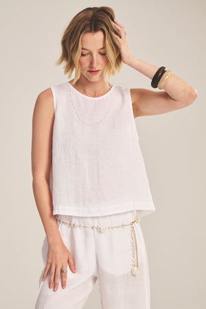 A woman stands against a plain background wearing the MAXINE LINEN TOP by Velvet by Graham & Spencer—a sleeveless, lightweight blouse paired with matching white pants and layered jewelry for breezy summer style.