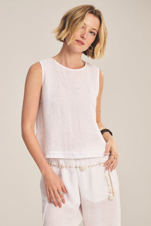 A woman with short blonde hair wears the MAXINE LINEN TOP by Velvet by Graham & Spencer and matching pants, accessorized with a delicate chain necklace and a pearl belt.