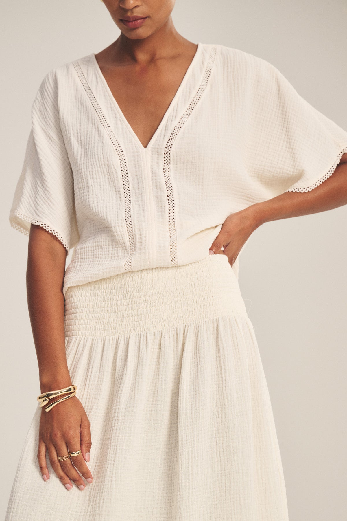 A woman wears the MAZIE SKIRT by Velvet by Graham & Spencer with a textured cream short-sleeve blouse, lace trim, and gold accessories.-41296919855297