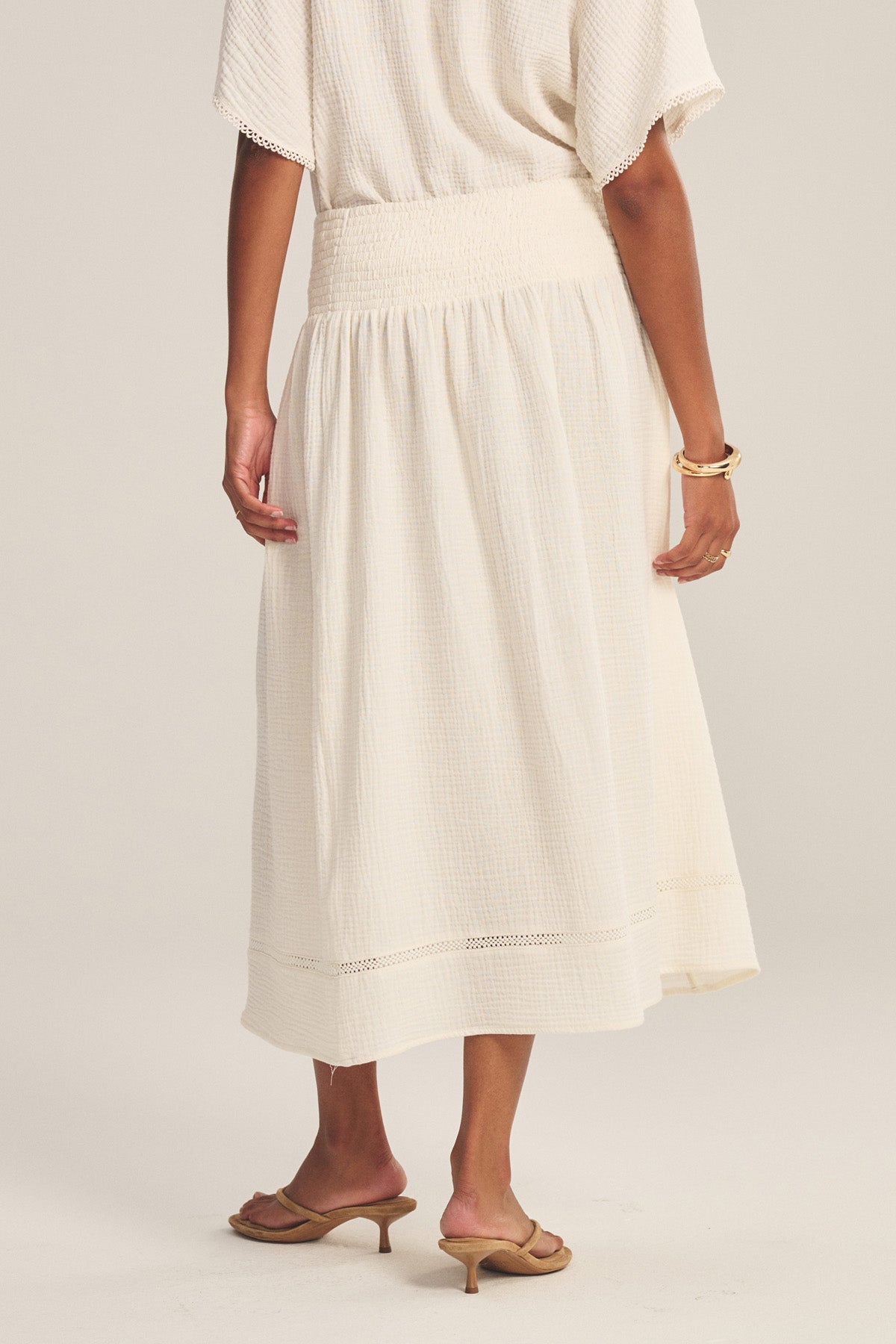 A person wears the MAZIE SKIRT by Velvet by Graham & Spencer with a matching top, tan heeled sandals, and gold bracelets, standing against a neutral background.