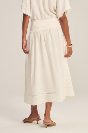 A person wears the MAZIE SKIRT by Velvet by Graham & Spencer with a matching top, tan heeled sandals, and gold bracelets, standing against a neutral background.