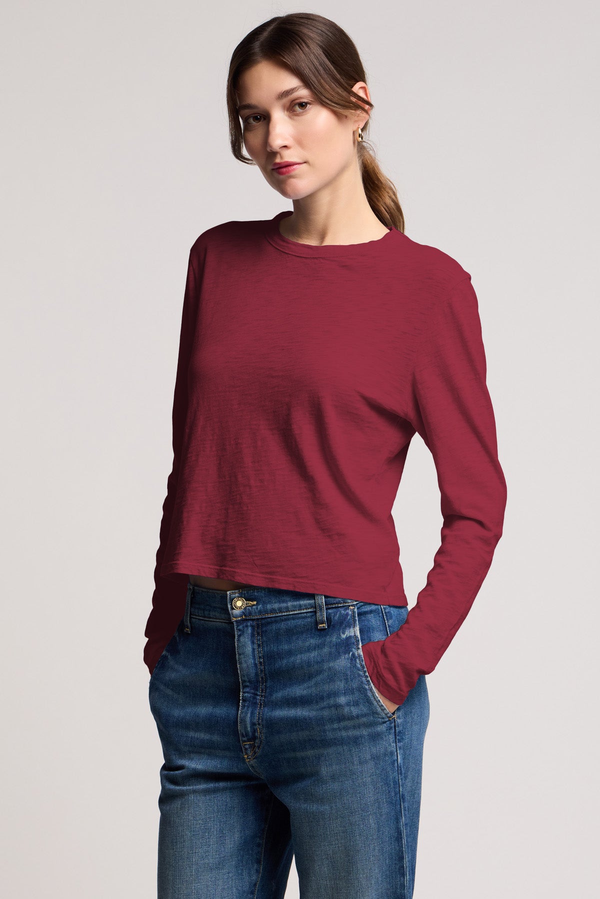 A woman stands with her hands in her jean pockets, wearing the MEGAN TEE by Velvet by Graham & Spencer—a textured maroon cotton slub long-sleeve—while looking at the camera against a plain background.