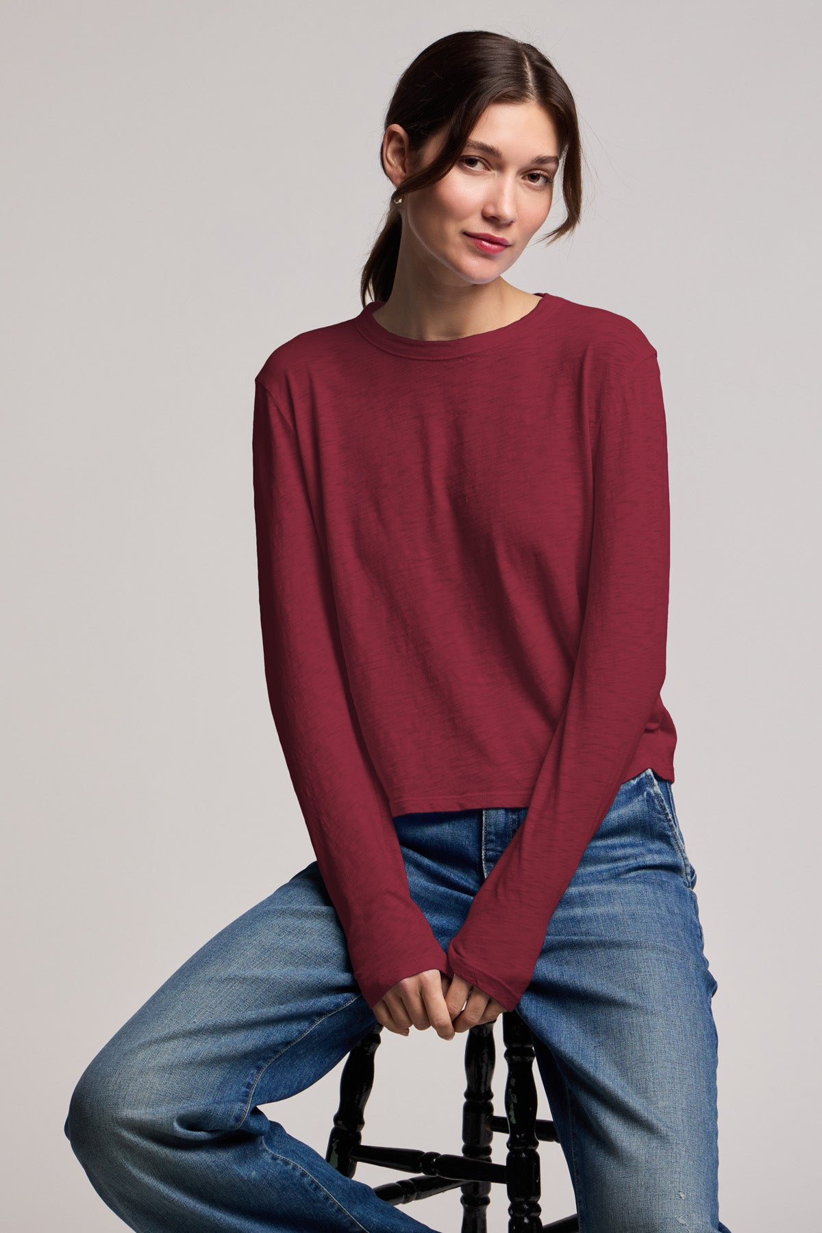 A woman wearing the MEGAN TEE by Velvet by Graham & Spencer and blue jeans sits on a black stool against a plain light background.-40430945468609