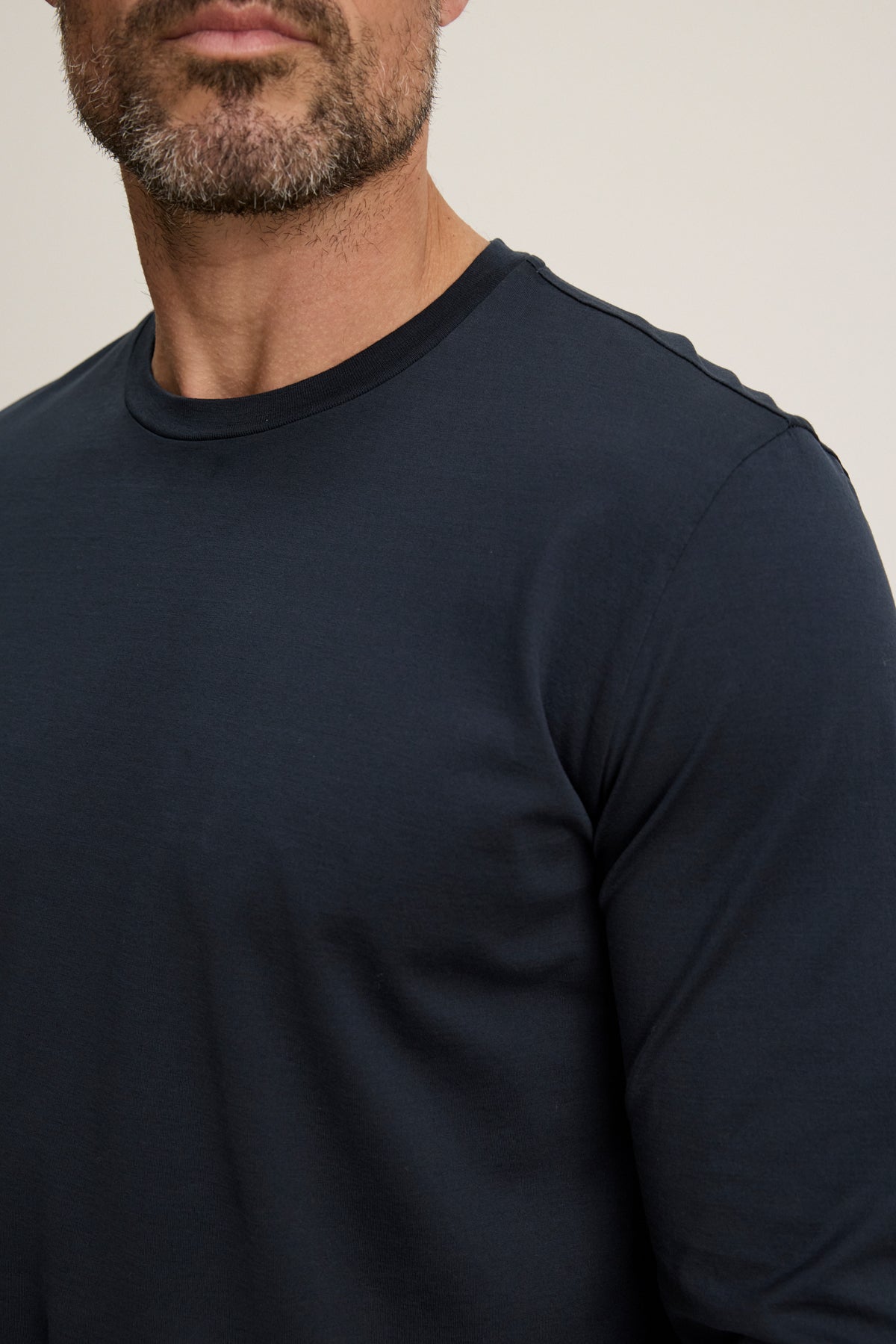 A man with a short beard wears the ALFIE TEE by Velvet by Graham & Spencer—a tailored-fit, dark navy long sleeve crafted from midweight mercerized cotton—standing against a plain light background.-39450513309889
